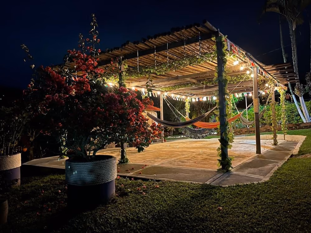 Pérgola con hamacas y luces de noche, rodeada de jardín
